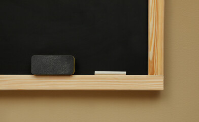Clean blackboard with chalk and duster hanging on beige wall