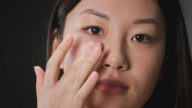 Skin moisturizing concept. Young asian woman applying nourishing cream on her under eye area, skin lifting procedures