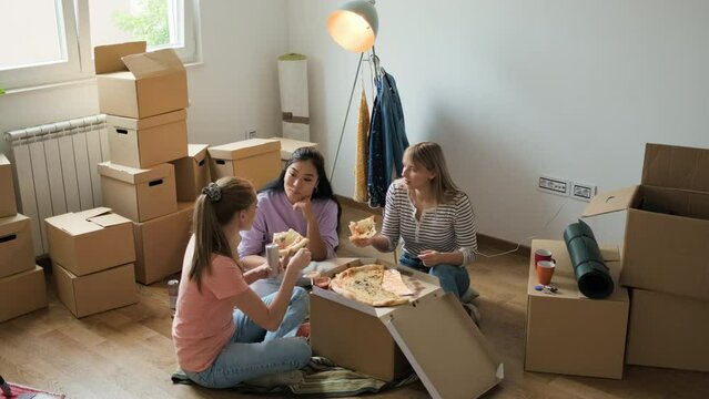 Female friends eating pizza after bringing the boxes into the new apartment.