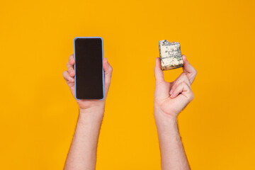 Photo of male hands holding a slice of gorgonzola cheese and a cellphone