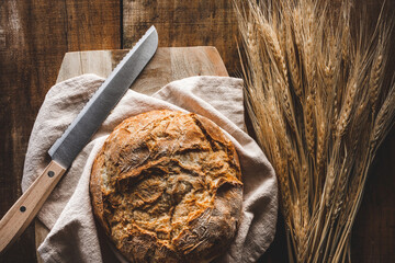 vista superior de una hogaza de pan con un cuchillo sobre una tabla de cortar, con espigas de...