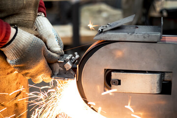 A factory worker grinds a product on an electric grinder, sparks fly. Metalworking steel close-up. 