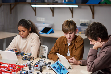 Group of teenagers using digital tablets to project robots with artificial intelligence while sitting at the table