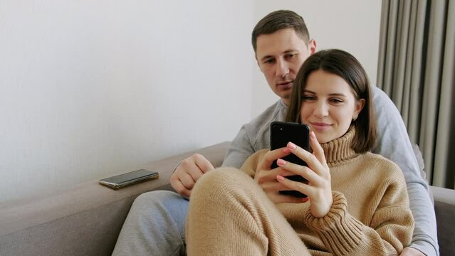 Guy helps girl with choice using mobile phone. Buying goods on Internet, choosing a gift, joint purchases.