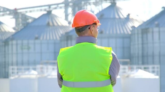 Grain silo containers cargo docks. Inspector stands at construction site looking at modern warehouse in large marine port backside view