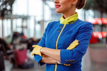 Close up of female flight attendant wearing aviation air hostess uniform and gloves while keeping arms crossed and smiling