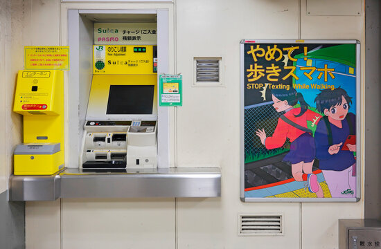 tokyo, japan - november 18 2021: Fare adjustment machine in a japanese train station and a prevention poster illustrating a passenger falling down on track with the words 'stop texting while walking'.