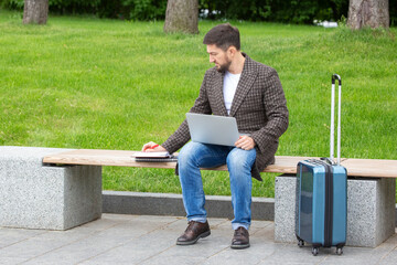 Successful businessman sits on a city bench and is engaged in business with documents and laptop