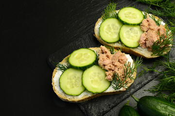 Sandwiches with tuna soft curd cheese and cucumber slices and dill on a black stone plate on a black background, copy space. Healthy food