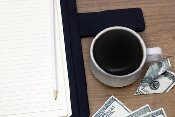 Notepad for notes with a pencil and a cup of coffee, banknotes are scattered on the table. business and finance concept.