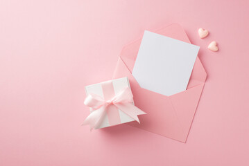 Top view photo of woman's day composition white giftbox with pink silk ribbon bow open pink envelope with paper sheet and two small hearts on isolated pastel pink background with blank space