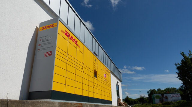 DHL pickup location German name: Packstation, logistics company Deutsche Post DHL Group, blue sky.
