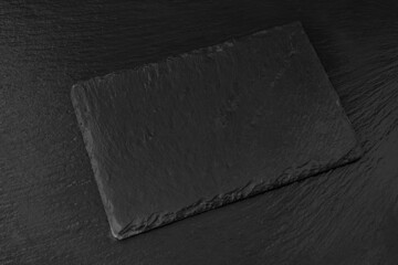 Black slate board or plate on dark stone texture background top view. Empty space for food, sushi, text, menu