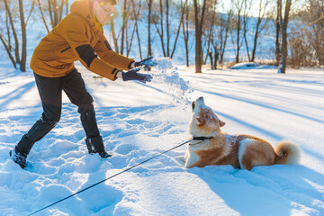 Young man with Akita Inu dog in park. Snowy winter background. Sunny day. The concept of friendship between a man and a dog.