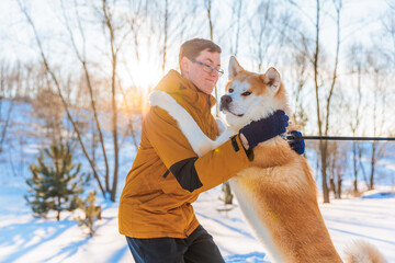 Young man with Akita Inu dog in park. Snowy winter background. Sunny day. The concept of friendship between a man and a dog.