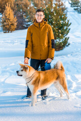 Young man with Akita Inu dog in park. Snowy winter background. Sunny day. The concept of friendship between a man and a dog.