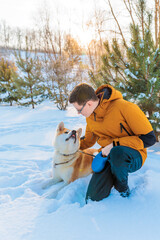 Fototapeta na wymiar Young man with Akita Inu dog in park. Snowy winter background. Sunny day. The concept of friendship between a man and a dog.