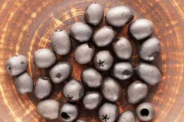 Some pickled black olives on a clay dish, macro, top view.
