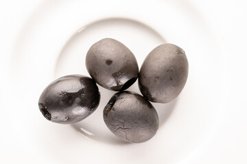 A few pickled black olives on a white ceramic saucer, macro, top view.