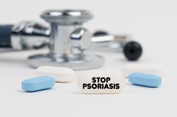 Obraz na płótnie Canvas On a white surface lie pills, a stethoscope and a tablet with the inscription - STOP PSORIASIS