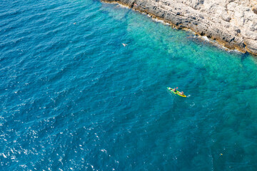 Top view of sportsmen or tourists kayaking in the turquoise transparent blue water of Adriatic sea rocky shore. Summer leisure activity in the canoe. 