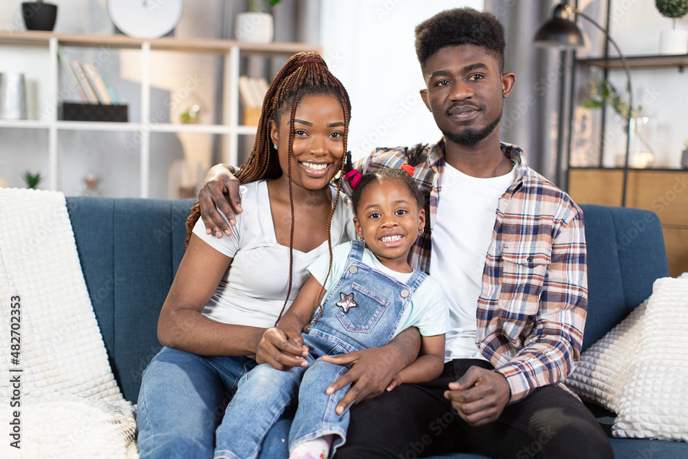 Wall mural beautiful african american family of three relaxing together on cozy sofa at modern apartment. young