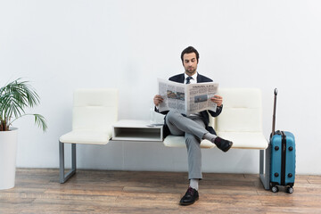 man reading newspaper in departure lounge near suitcase.