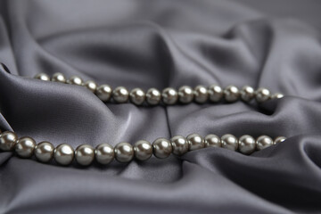 Fototapeta premium Beautiful silver pearls on grey silk, closeup