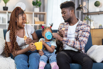 Positive young parents eating croissants and drinking tea with their little daughter on comfy...