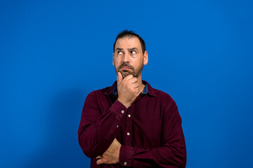 Thinking man isolated on blue background. Closeup portrait of a casual young pensive businessman looking up at copy space. Caucasian male model