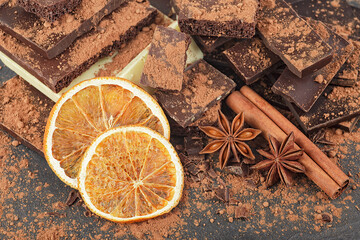 Broken chocolate pieces, cocoa powder, spices and dried oranges on a black background
