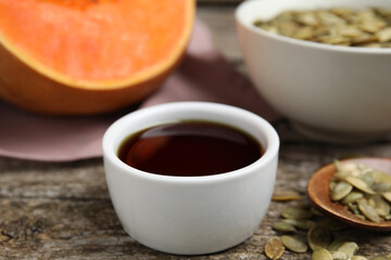 Bowl of pumpkin oil and seeds on wooden table, closeup