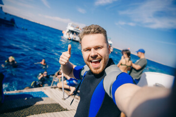 Selfie happy tourist man diver in wetsuit is preparing to dive into sea on boat. Concept diving trip Egypt - obrazy, fototapety, plakaty