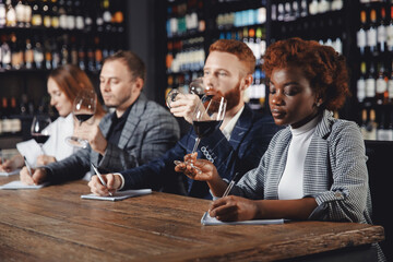 African woman tasting red wine sommeliers and taking notes at degustation notepad
