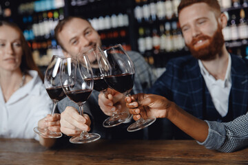 Concept Multicultural friendship, closeup hands of African woman and European men are checked with glasses of red wine in restaurant
