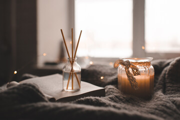 Bamboo sticks in bottle with scented candles and open book on wooden tray in bed closeup. Home...