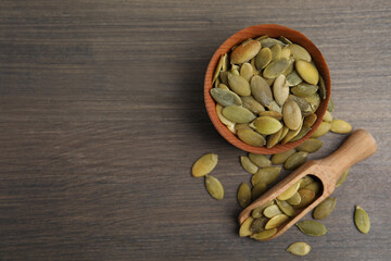 Bowl and scoop with pumpkin seeds on wooden table, flat lay. Space for text