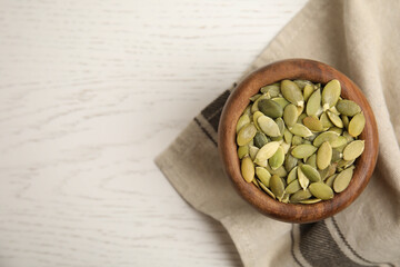 Bowl of pumpkin seeds with napkin on white wooden table, top view. Space for text