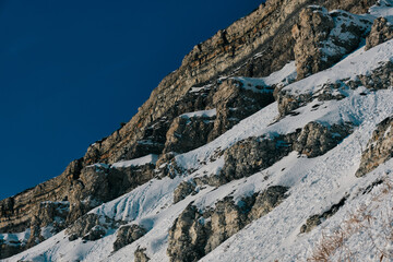 A snow-covered cliff with grass growing from under the snow at its foot