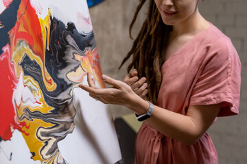 Close-up of young artist pointing at painted picture and talking about it during presentation in...