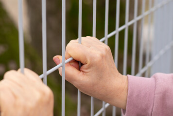 Woman's hands holding a metal fence. The concepts of human rights day, female refugee help, freedom, and justice. A close-up.