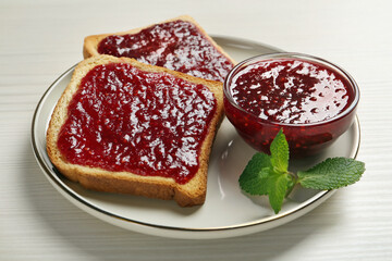 Delicious toasts served with jam and mint on white wooden table, closeup