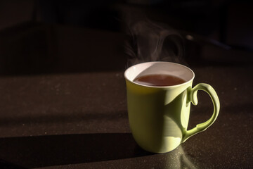 Green cup with hot tea in the sunlight. Lifestyle domestic photo concept. Minimalistic composition with copy space for text. Breakfast time with tasty warm drink