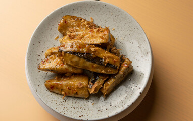 Caramelized fried bananas presented on a round gray plate close up on a brown background. Crispy banana pieces fried in butter and sugar. Restaurant serving food, sweet Thai dessert. Asian cuisine.