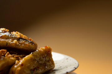 Caramelized fried bananas presented on a round gray plate close up on a brown background. Crispy banana pieces fried in butter and sugar. Restaurant serving food, sweet Thai dessert. Asian cuisine.