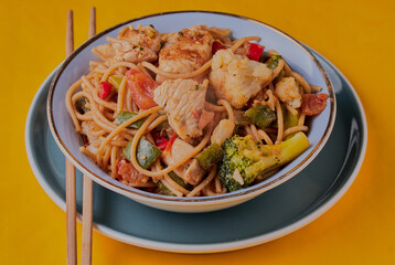 Chicken chow mein with chopsticks on a yellow background.