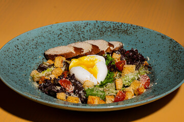 Fresh caesar salad with duck, tomato, lettuce, croutons, cheese and sliced poached egg on top. Vegetable juicy salad with meat and tasty sauce on gray plate close up. Healthy food, restaurant dish.