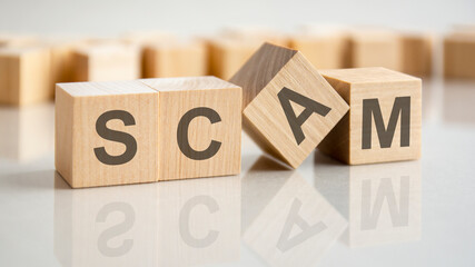 four wooden blocks with the letters scam on the bright surface of a gray table, business concept