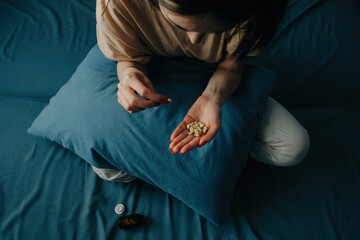 Sad young unrecognizable woman takes antidepressants. A young woman sits on a bed with pills in her...