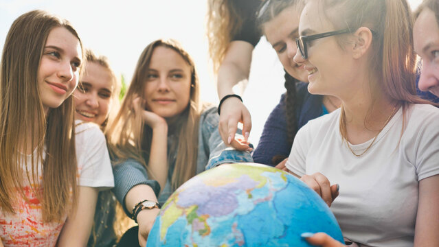A group of cheerful girls is exploring the globe of the world in the meadow.